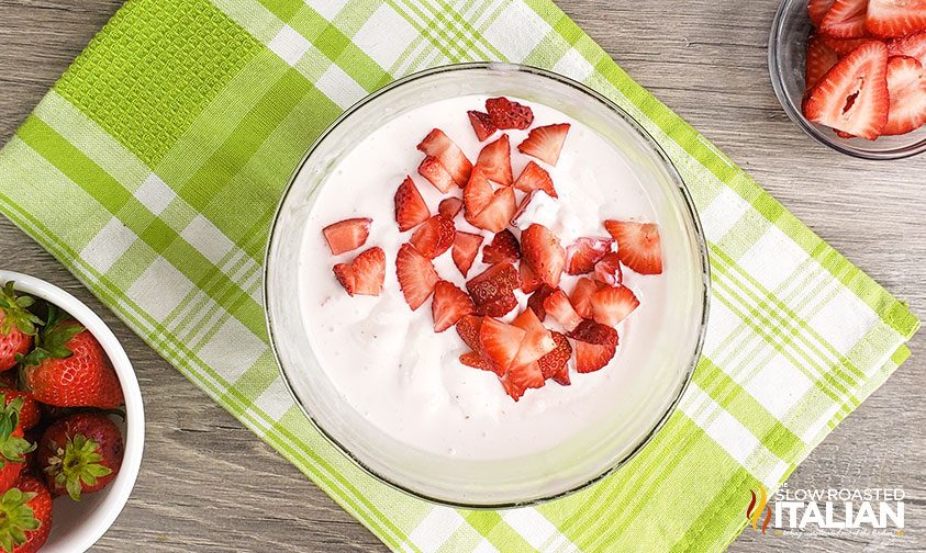 chopped fresh strawberries in a bowl of softened ice cream