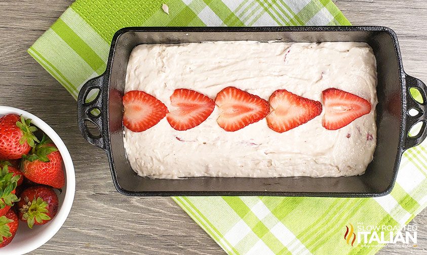 ice cream bread batter smoothed into a cast iron loaf pan with a line of sliced strawberries down the middle