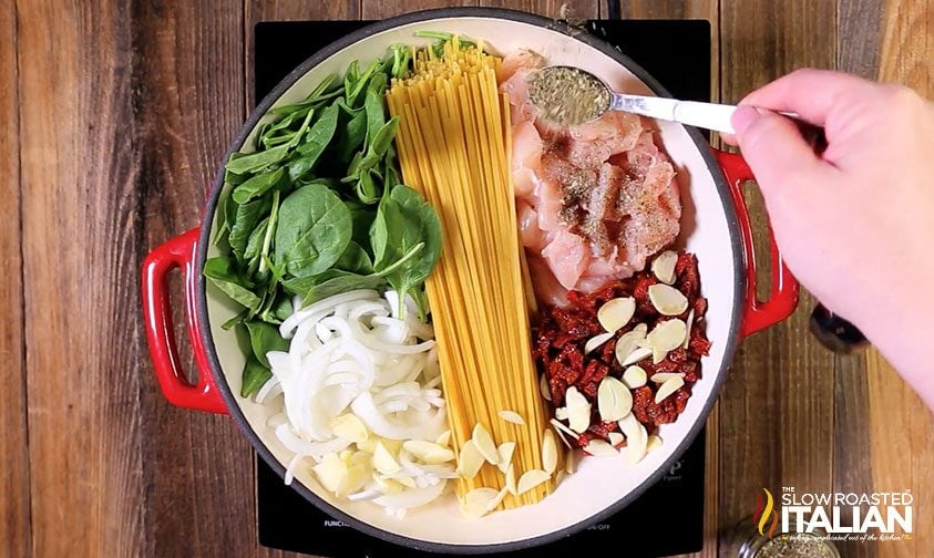 adding seasoning to pot of uncooked linguine and vegetables