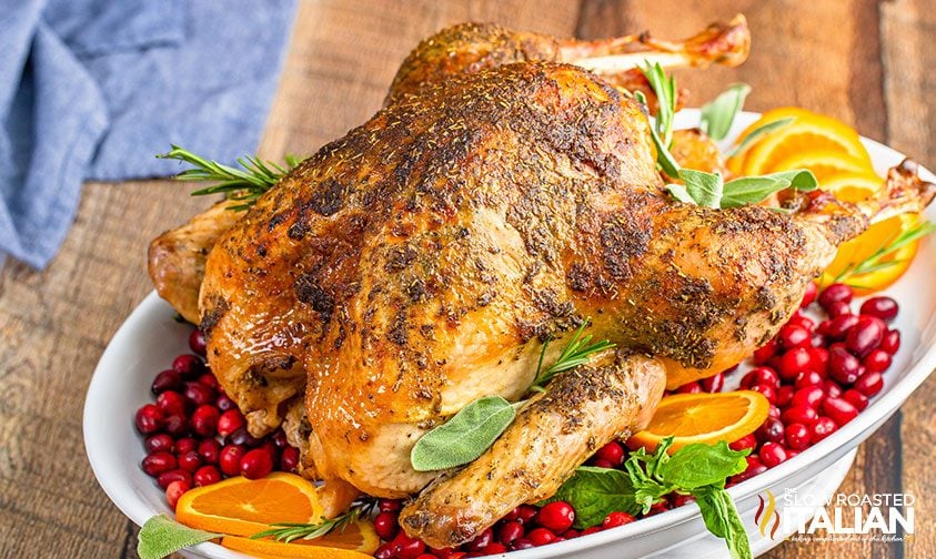 slow roasted turkey on platter with cranberries, orange slices, and fresh herbs