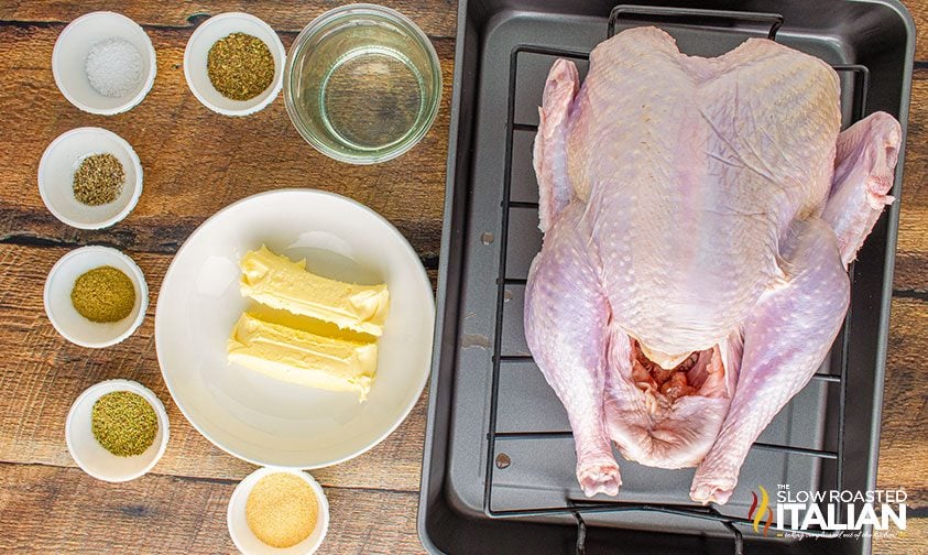 uncooked turkey in roasted pan next to herb butter ingredients