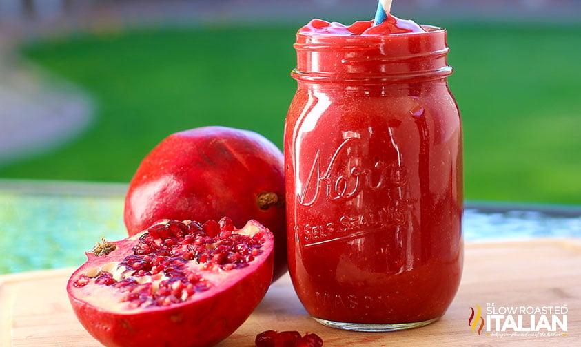 pomegranate smoothie in a glass with a slice open pomegranate