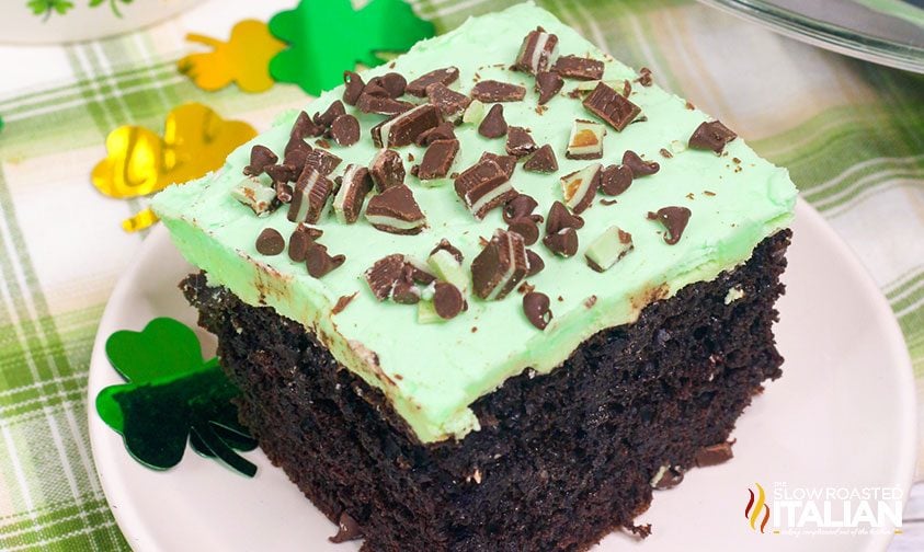 slice of mint chocolate poke cake topped with minty green frosting and chopped Andes candies