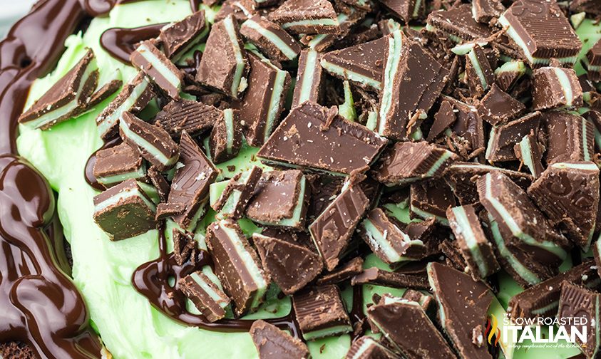 close up: chopped Andes mints and chocolate drizzle on top of mint chocolate layer cake