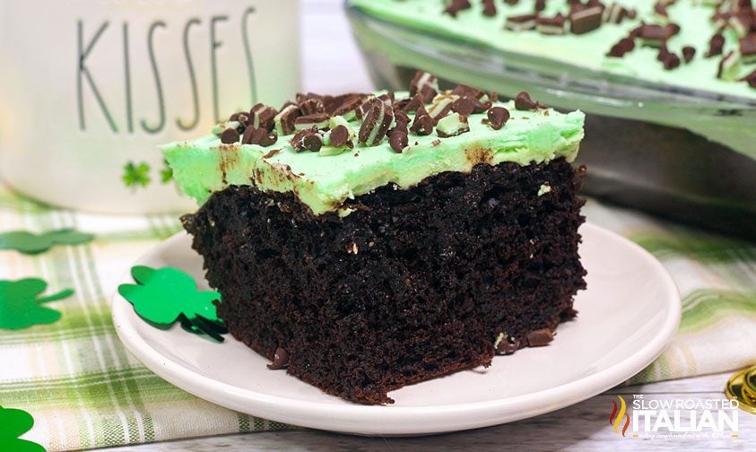 side view of a slice of chocolate poke cake with green frosting and candy on top