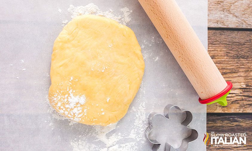 disc of sugar cookie dough on parchment with rolling pin and shamrock cutter