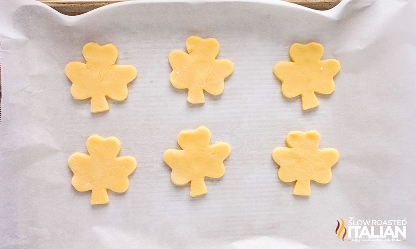 cut out shamrock cookies on parchment lined baking sheet