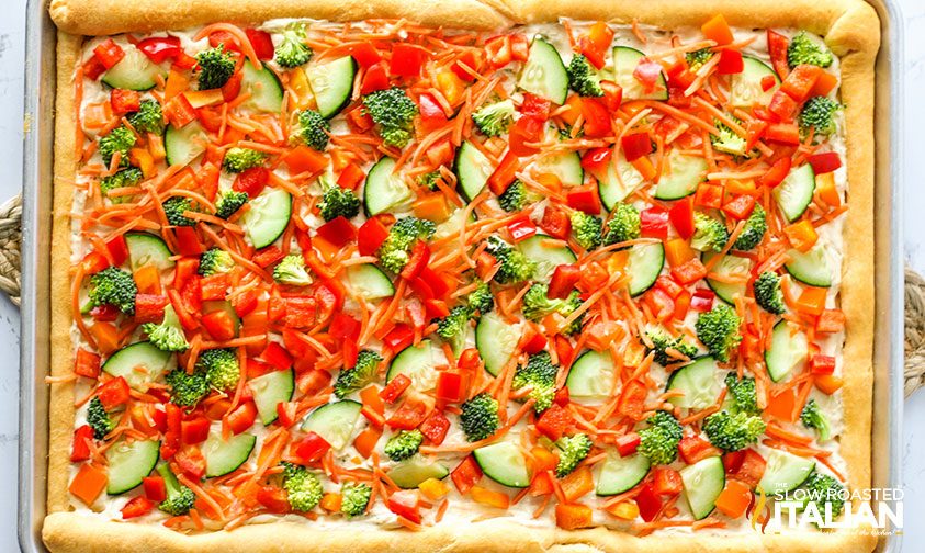 crescent roll pizza topped with hummus spread and fresh veggies