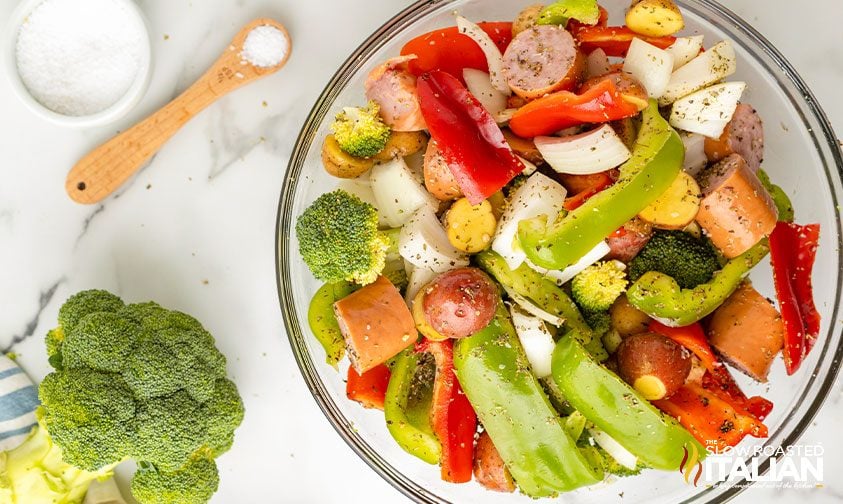 chopped sausage and veggies tossed with oil and seasonings in a bowl