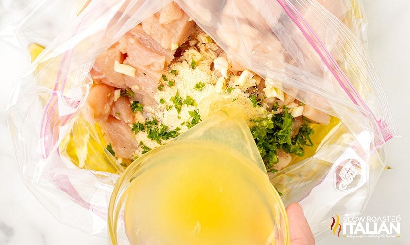 pouring lemon juice into ziploc bag of chopped chicken, garlic, and seasonings