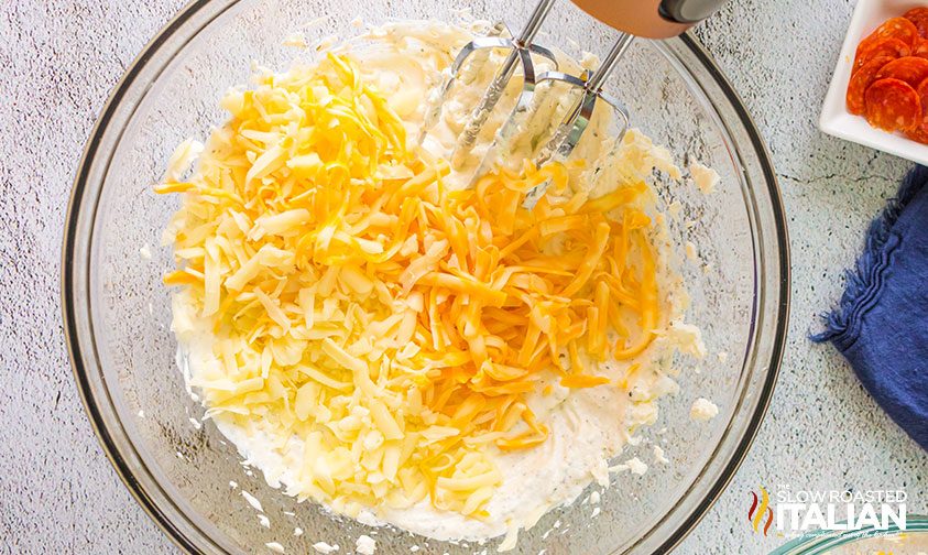 mixing shredded cheese with whipped cream cheese