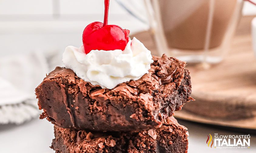 stacked brownies topped with whipped cream and a maraschino cherry