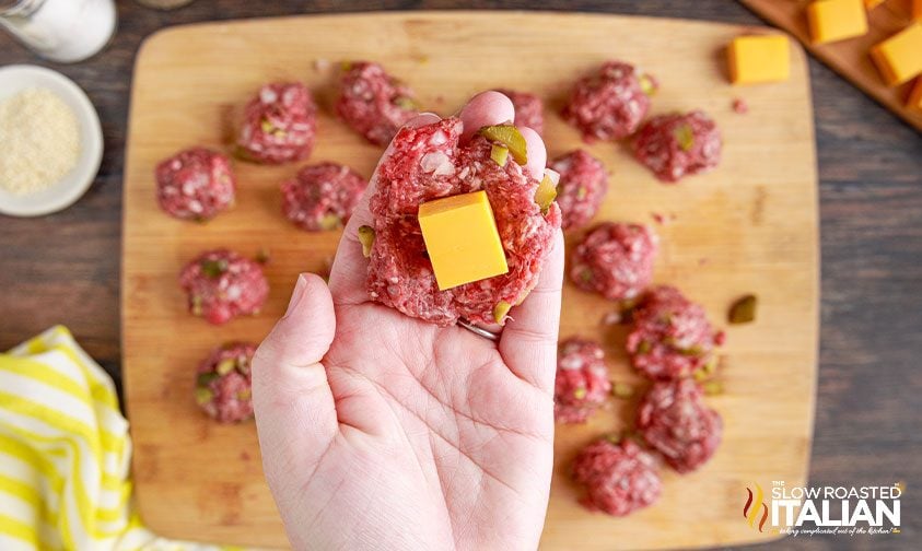 holding some flattened burger meat with cube of cheese in the middle