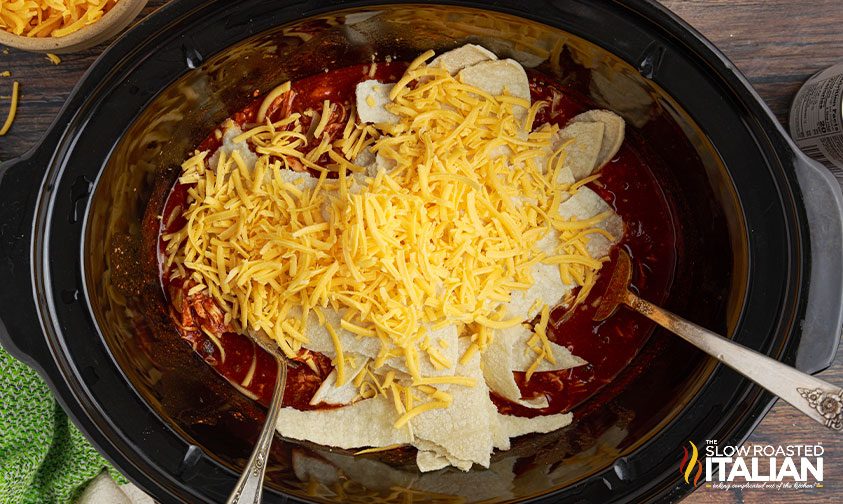 mixing shredded cheese and tortilla pieces into red enchilada chicken