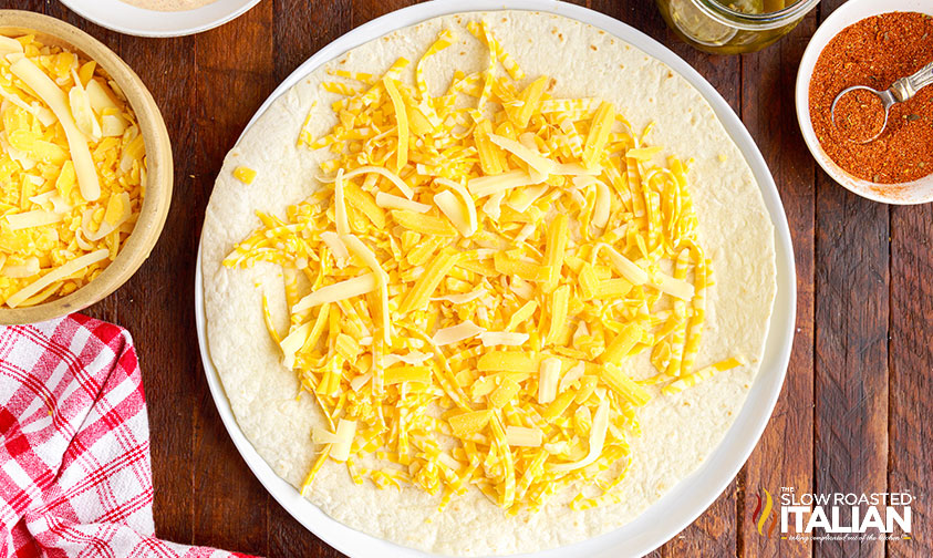 covering tortilla in shredded cheese