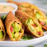 diagonally sliced avocado egg rolls on plate with dip