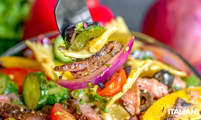 forkful of pasta salad with onions, peppers, and steak