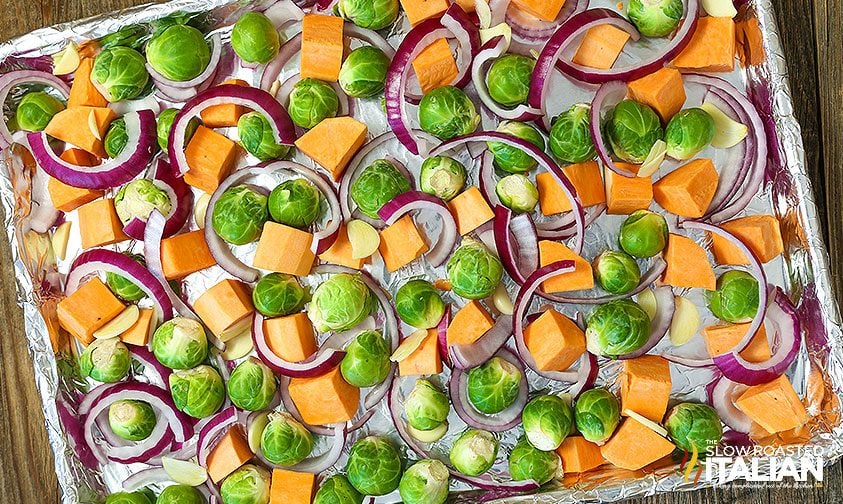 brussels sprouts, sweet potato chunks, and red onion on foil lined sheet pan