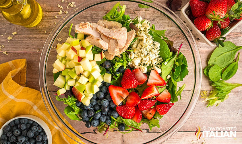 mixed greens, grilled chicken, apple, strawberries and blueberries in a salad bowl
