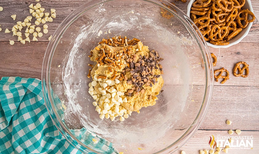 folding white chocolate chips, toffee bits and pretzels into cookie skillet dough