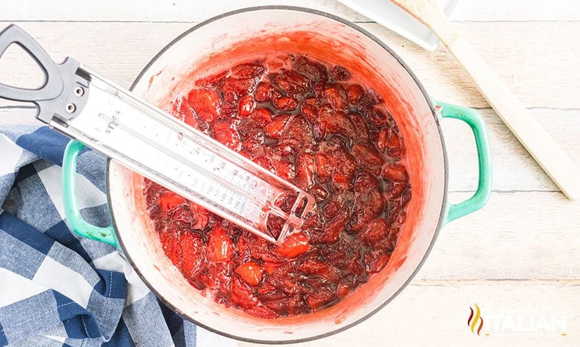 candy thermometer in a pot of strawberry jam
