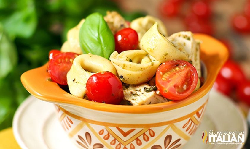 close up: tortellini with pesto, chicken, and tomatoes in bowl with orange designs