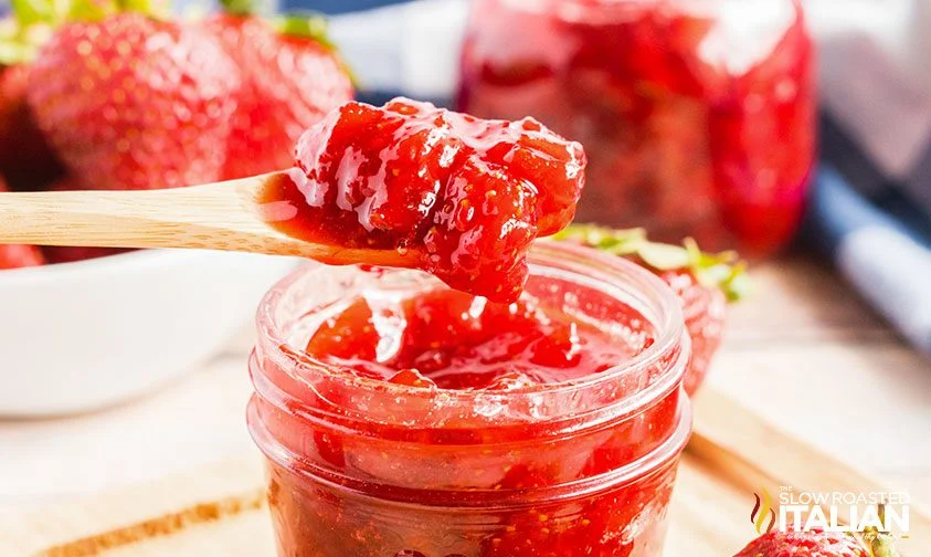 scooping strawberry jam from jar with wooden spoon