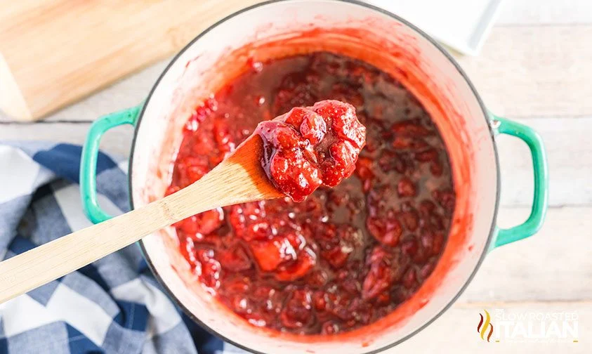 homemade strawberry jam on wooden spoon over pot