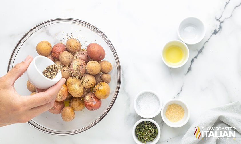 sprinkling seasonings over baby potatoes in bowl