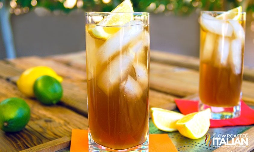 two long island iced tea cocktails surrounded by lemons and limes