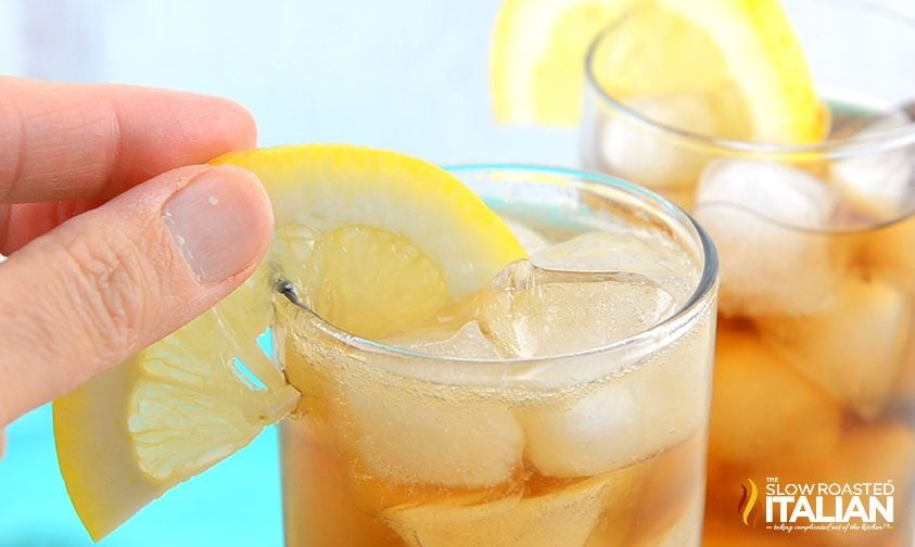 placing lemon slice on rim of glass filled with long island iced tea