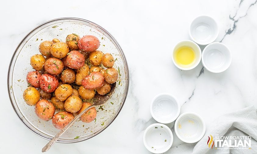 baby potatoes coated in oil and seasonings in clear bowl