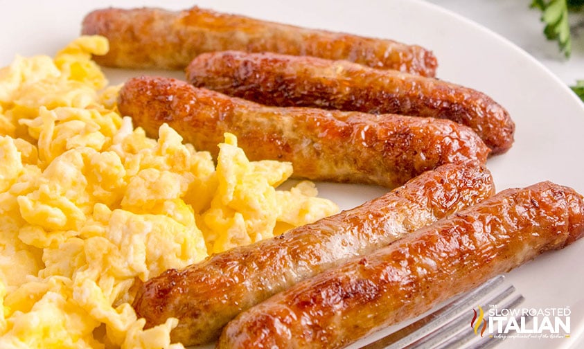 5 air fryer sausage links on a plate with scrambled eggs