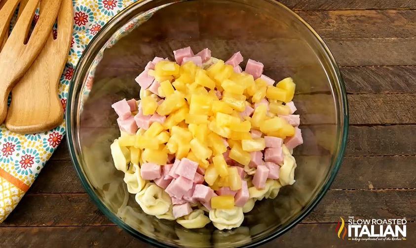 adding pineapple tidbits to ham and tortellini in a large mixing bowl