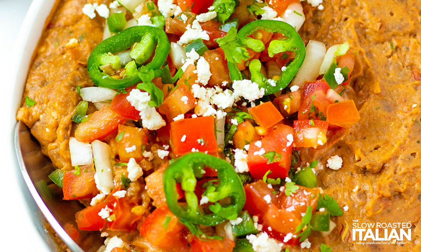 closeup of refried bean casserole topped with jalapenos and tomatoes