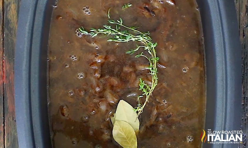 thyme and bay leaves on top of onion soup in slow cooker