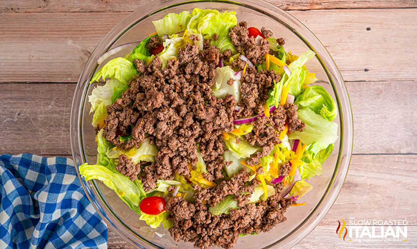 adding ground beef to salad in a bowl