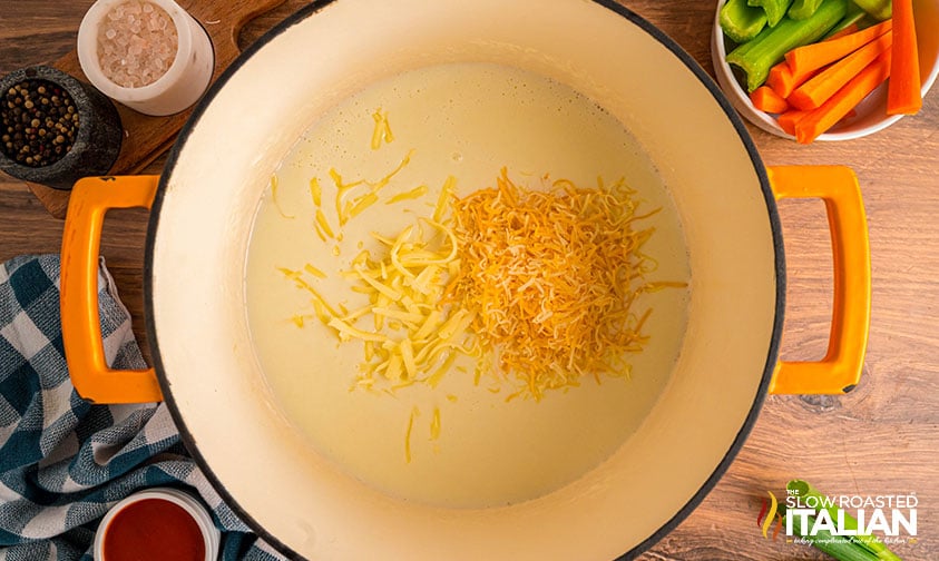 adding shredded cheese to sauce in large pot