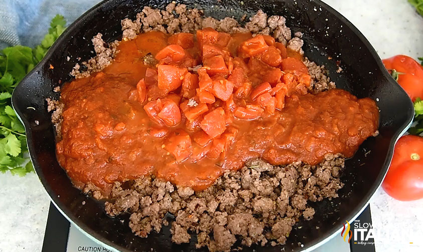 adding tomatoes and sauce to browned beef in skillet