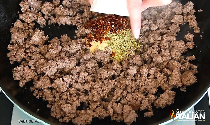 adding seasoning to browned ground beef in a skillet