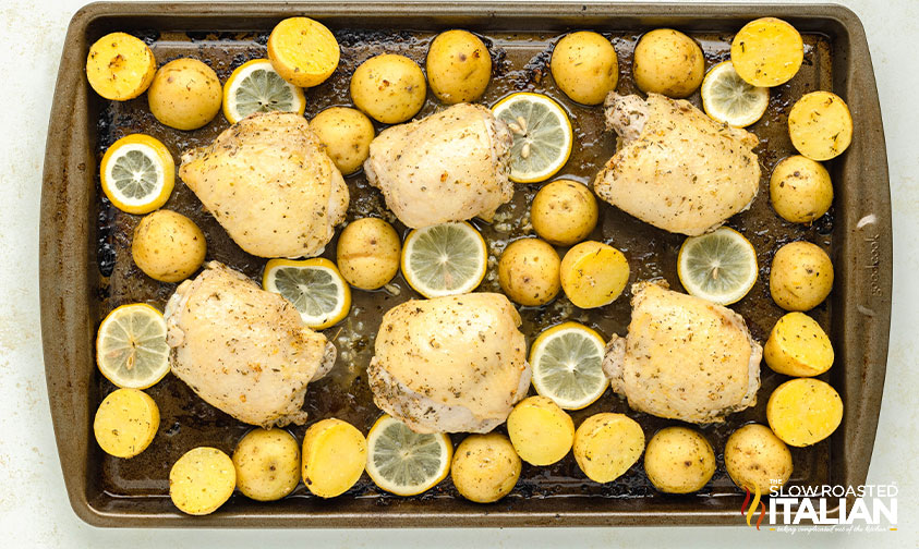 chicken, potatoes and lemon slices on a baking sheet