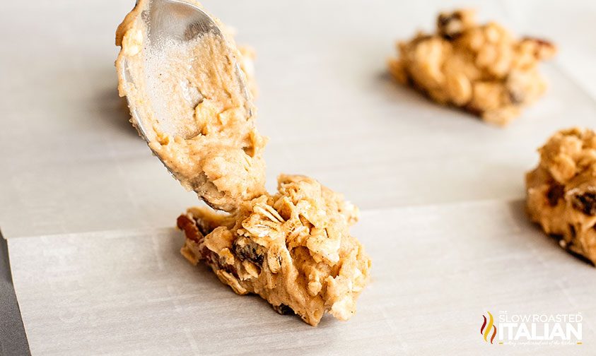 dropping spoonful of oatmeal cookie dough onto parchment lined baking sheet