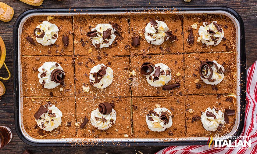 pan of tiramisu sliced into squared with whipped cream and chocolate shavings on top