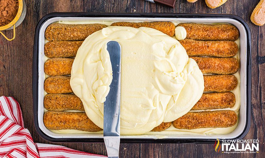 spreading custard over ladyfingers in pan