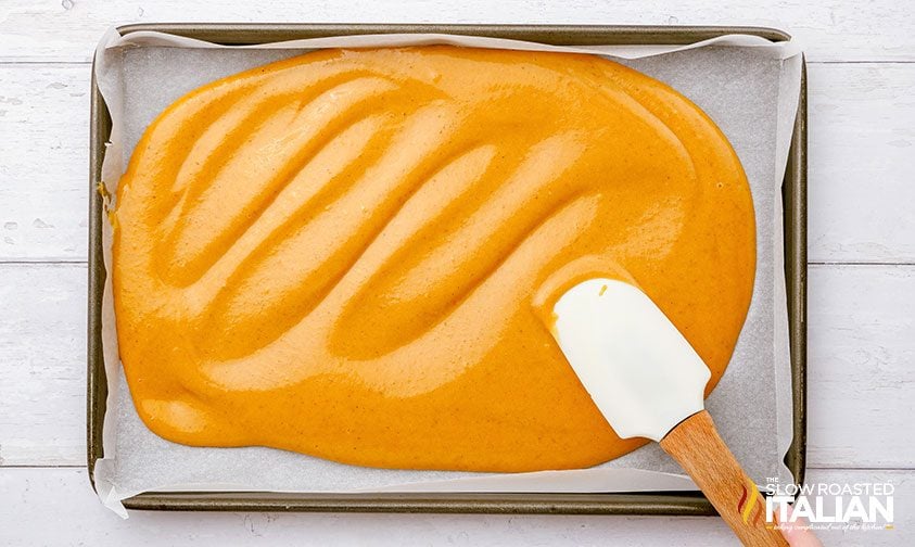 spreading pumpkin cake batter onto parchment lined jelly roll pan