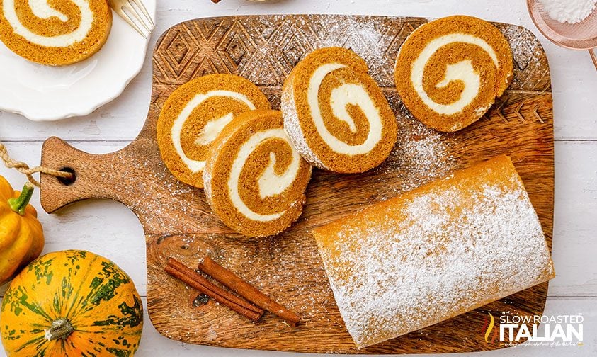 sliced pumpkin roll cake on cutting board, dusted with powdered sugar