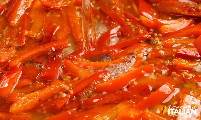 pouring white wine over bell pepper strips in skillet