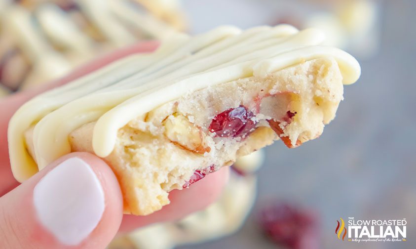 holding white chocolate cranberry shortbread cookie with bite taken out of it