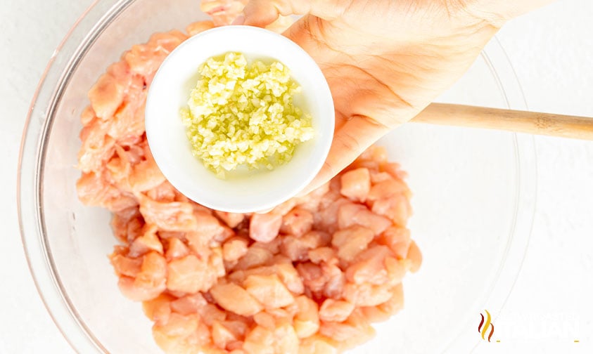 adding minced garlic to chopped chicken