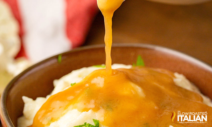 drizzling keto brown gravy over mashed potatoes in a bowl